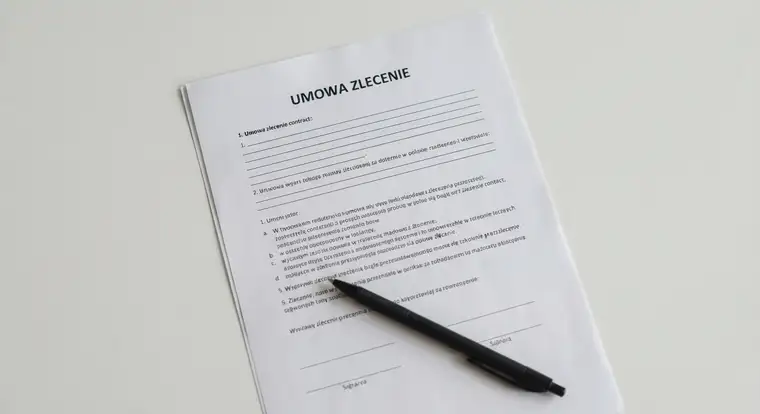 Osoba podpisująca umowę zlecenie przy biurku, obok leżą dokumenty i kalkulator do wyliczenia składek ZUS, umowa zlecenie jest korzystna dla pracodawcy
